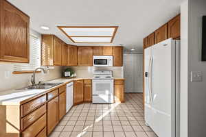 Kitchen featuring white appliances, light tile patterned floors, light countertops, brown cabinetry, and a textured ceiling