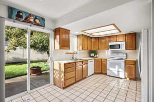 Kitchen with light countertops, light tile patterned floors, white appliances, and brown cabinetry