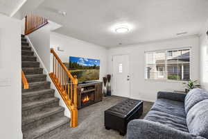 Living room with a textured ceiling, carpet, crown molding, and stairway