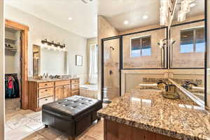 Full bath with a garden tub, two vanities, a stall shower, a walk in closet, and stone tile flooring