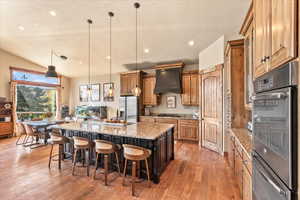 Kitchen with pendant lighting, light stone countertops, a kitchen bar, a large island with sink, and stainless steel appliances