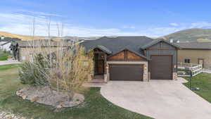 Craftsman-style house featuring an attached garage, a mountain view, stone siding, concrete driveway, and a front yard