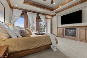 Primary Bedroom featuring multiple windows, ornamental molding, carpet, a ceiling fan, and a glass covered fireplace