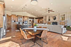 Dining space with vaulted ceiling, light wood-style flooring, ceiling fan, recessed lighting, and a stone fireplace