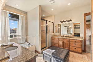 Bathroom with two vanities, a garden tub, a shower stall, recessed lighting, and stone tile floors