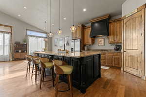 Kitchen featuring light stone countertops, a kitchen bar, two tone color scheme, light wood finished floors, and vaulted ceiling