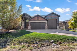 Craftsman house with an attached garage, stone siding, driveway, and a front yard