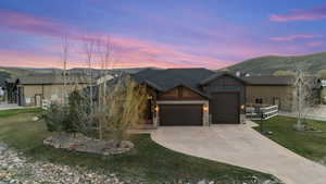 Craftsman inspired home with an attached garage, stone siding, driveway, a front lawn, and a mountain view