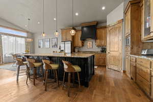 Two tone kitchen with a large island, vaulted ceiling, a kitchen bar, light wood finished floors, and light stone counters