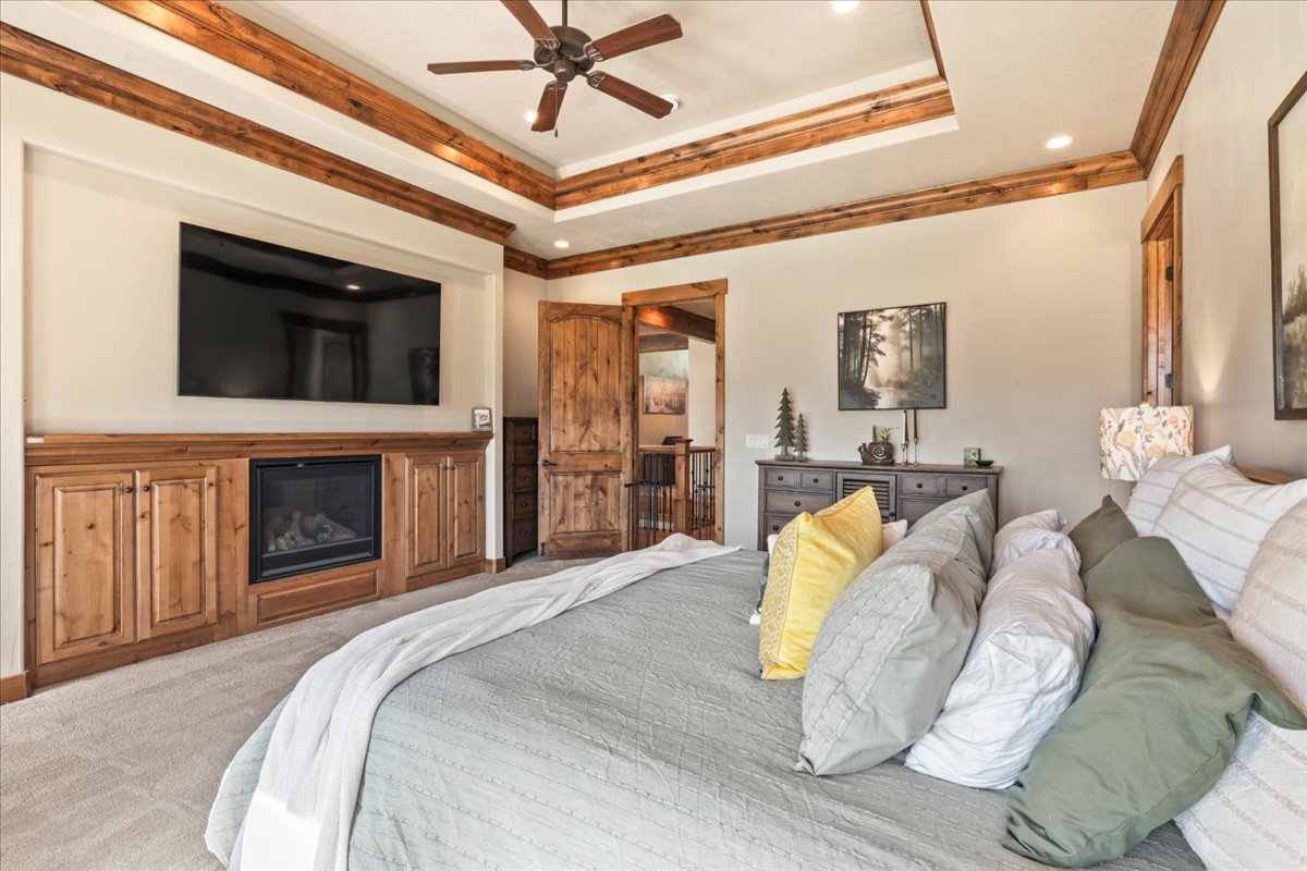 Primary Bedroom with a raised ceiling, crown molding, ceiling fan, and a glass covered fireplace