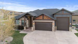 Craftsman-style house with a garage, concrete driveway, a shingled roof, and stone siding