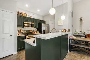 Kitchen with green cabinetry, tasteful backsplash, appliances with stainless steel finishes, decorative light fixtures, and a peninsula