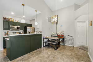 Kitchen with light countertops, a peninsula, hanging light fixtures, appliances with stainless steel finishes, and tasteful backsplash