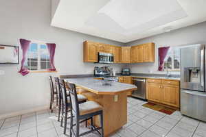 Kitchen with appliances with stainless steel finishes, light tile patterned floors, a breakfast bar, and brown cabinets