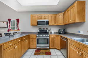 Kitchen with stainless steel appliances, light tile patterned floors, and brown cabinets