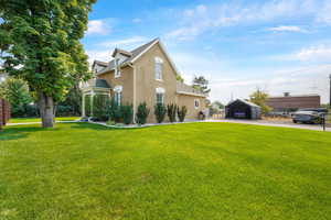 View of front of house featuring a front yard, stucco siding, a detached carport, and driveway