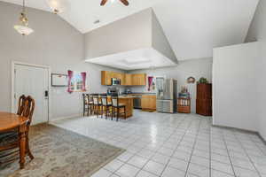 Kitchen with a kitchen breakfast bar, stainless steel appliances, light tile patterned floors, decorative light fixtures, and ceiling fan