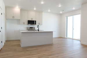 Kitchen featuring stainless steel appliances, light wood-type flooring, a center island with sink, recessed lighting, and white cabinets