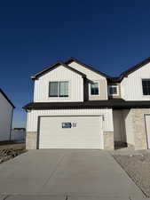 Modern farmhouse with stone siding, driveway, an attached garage, and board and batten siding