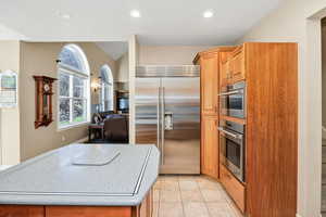 Kitchen with appliances with stainless steel finishes, light tile patterned floors, recessed lighting, brown cabinets, and lofted ceiling