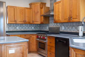 Kitchen featuring wall chimney range hood, backsplash, premium range, and light tile patterned flooring