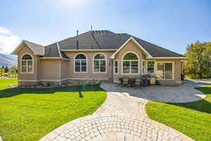 Rear view of house with stucco siding, a lawn, a patio, and a shingled roof