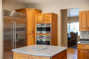 Kitchen with stainless steel appliances, a textured ceiling, brown cabinetry, a chandelier, and light tile patterned floors