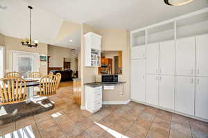 Kitchen with side room with white cabinetry, decorative light fixtures, light tile patterned floors, black microwave, and recessed lighting