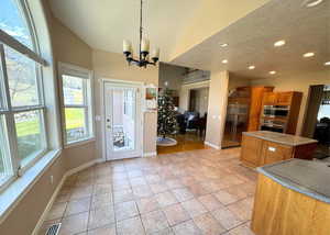 Kitchen featuring a textured ceiling, brown cabinets, pendant lighting, stainless steel appliances, and a chandelier