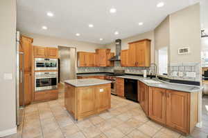 Kitchen with decorative backsplash, a kitchen island, high quality appliances, brown cabinets, and light tile patterned flooring