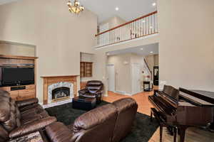 Living room with light wood-style floors, a towering ceiling, a premium fireplace, recessed lighting, and a chandelier