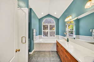 Primary Bathroom featuring lofted ceiling, double vanity, a shower stall, a garden tub, and light tile patterned flooring