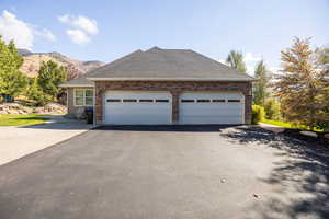 View of side of property featuring driveway, a garage, brick siding, a shingled roof, and a mountain view