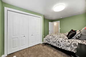 Bedroom with dark colored carpet, a textured ceiling, and a closet