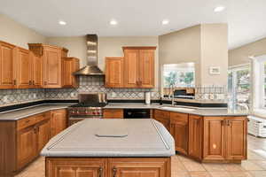 Kitchen featuring light tile patterned floors, brown cabinets, a kitchen island, wall chimney range hood, and recessed lighting
