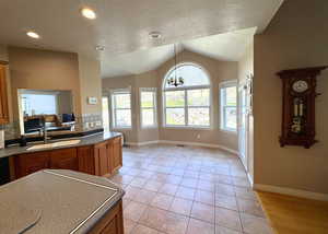 Kitchen with a textured ceiling, brown cabinets, a chandelier, light tile patterned floors, and vaulted ceiling