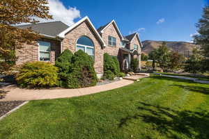 View of front facade featuring a large front lawn, brick exterior, roof with shingles, and a mountain view