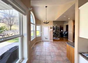 Foyer with a textured ceiling, lofted ceiling, light tile patterned floors, and a chandelier