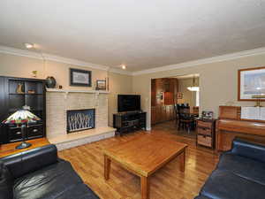 Living room featuring wood finished floors, a fireplace, ornamental molding, and a textured ceiling