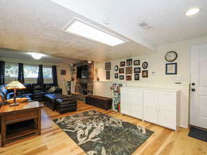 Living room featuring a textured ceiling, light wood-type flooring, and a stone fireplace