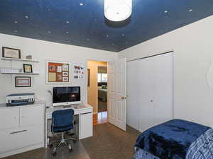Bedroom featuring a desk, dark colored carpet, and a closet