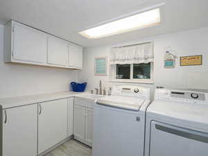 Laundry area featuring separate washer and dryer, cabinet space, and light wood-style floors