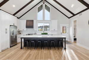 Kitchen with white cabinets, a breakfast bar area, high vaulted ceiling, a large island, and stainless steel fridge