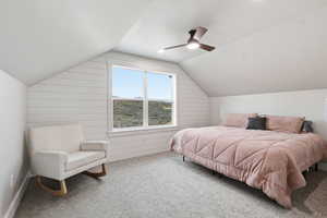 ABOVE GARAGE: Carpeted bedroom featuring vaulted ceiling, a ceiling fan, and wood walls