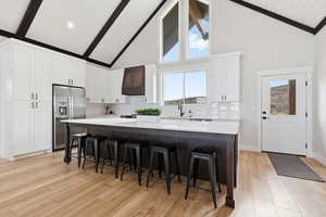 Kitchen with tasteful backsplash, white cabinetry, high vaulted ceiling, a kitchen bar, and stainless steel fridge with ice dispenser
