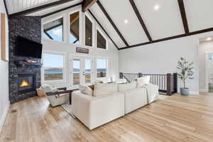 Living area with high 18' vaulted ceiling, LVP wood-style floors, a stone fireplace, and beamed ceiling