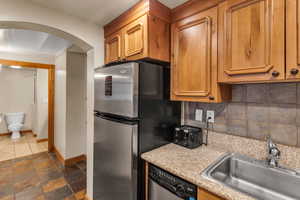 Kitchen with decorative backsplash, brown cabinets, appliances with stainless steel finishes, and dark stone finish floors