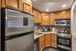 Kitchen with stainless steel appliances, backsplash, recessed lighting, dark stone finish floors, and brown cabinetry