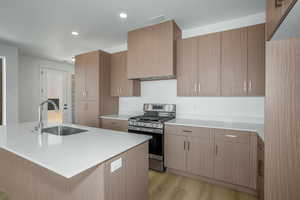 Kitchen with gas stove, a kitchen island with sink, light wood-style flooring, recessed lighting, and light stone countertops