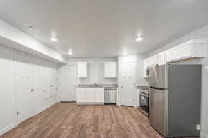 Kitchen with stainless steel appliances, white cabinetry, LVT flooring, recessed lighting, and light countertops